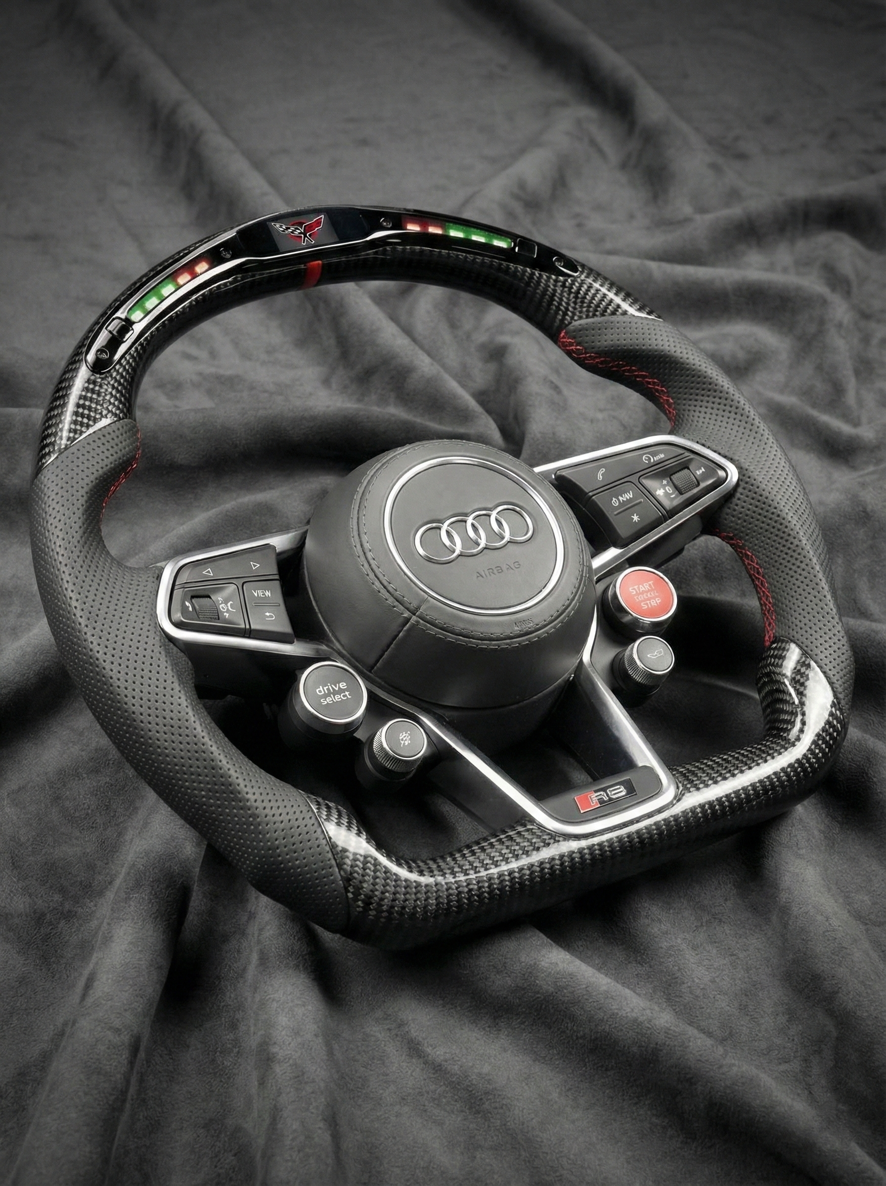 Carbon fiber steering wheel with Audi logo on a dark fabric background